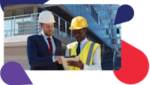 Two men in hard hats and suit and tie use project management software on tablet