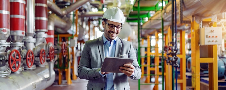 Man with helmet lookin into a tablet working in a plant 
